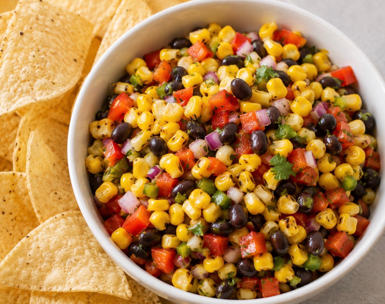 Homemade corn salsa with sweet corn, tomatoes, peppers, onions, and black beans served with tortilla chips.